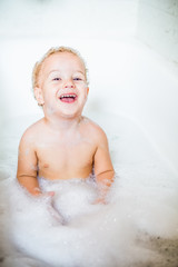 Cute two year old boy taking a relaxing bath with foam