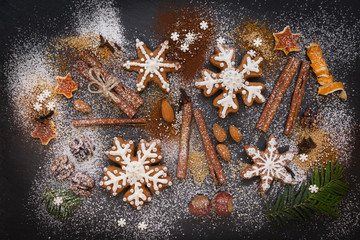 Obraz na płótnie Canvas Christmas or New Year background of Gingerbread cookies, spices, nuts with sugar and snowflakes. Top view on dark stone background