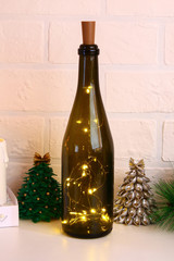 Garland in the bottle. Empty champagne bottle with garland inside on white table. Glowing decor for Christmas. Diy, handmade with their own hands