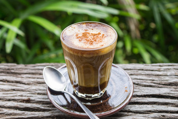 Latte Coffee in Glass with Spoon on Wood Table on Natural Green Tree Background