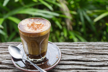 Latte Coffee in Glass with Spoon on Wood Table on Tree Background Left Zoom