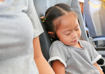 Obraz premium Cute little Asian child girl sleeping on the seat of airplane beside her mother.