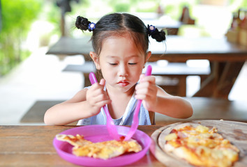 Little child girl enjoy eating pizza on the table.