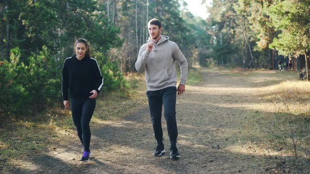 Cute couple young man and his girlfriend are doing sports in park together doing exercises simultaneously enjoying movement, nature and good company.