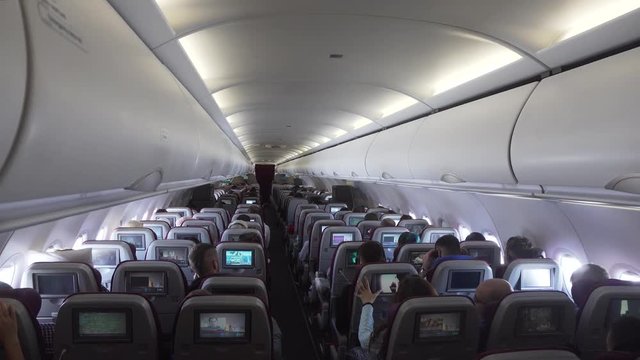 Interior passengers airplane with people on seats. Aircraft cabin with rows of seats. Passengers traveling by a modern commercial plane, inside of an airplane. Travel concept. 4K video.