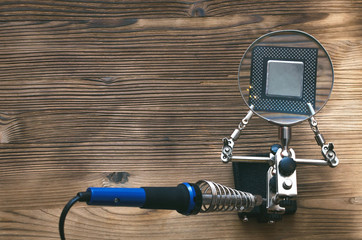 Retro computer CPU chip through magnifying glass mounted on the soldering stand and soldering iron...