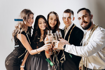 Beautiful young girls and guys dressed in stylish elegant clothes smile  together and clink glasses with champagne on a white background in the studio confiture around. Party time