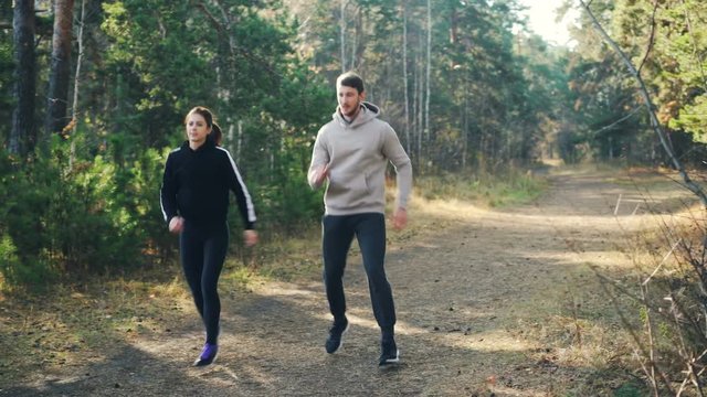 Happy couple young woman and her husband are doing sports in park jumping on the ground and smiling. Active lifestyle, modern youth and nature concept.