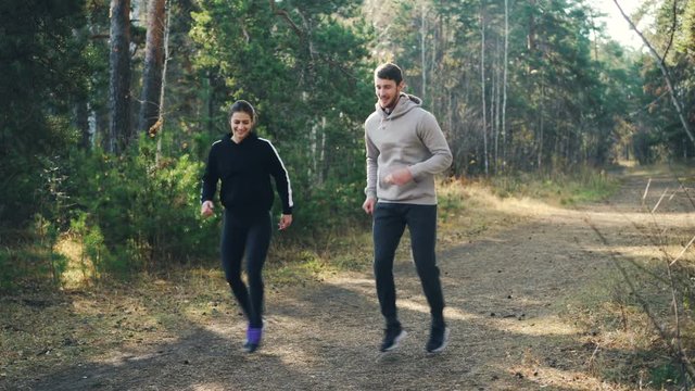 Smiling young people woman and man are jumping in forest doing sports wearing tracksuits and sneakers having fun and caring for health. Nature and exercises concept.