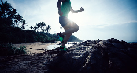 Woman trail runner running at rocky mountain top on seaside
