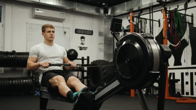Fitness young man using rowing machine in the gym crossfit training at night student professional athlete bodybuilder