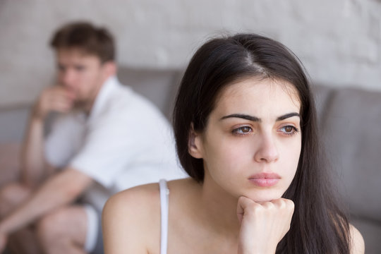 Frustrated young woman looking in distance, think about relationships, sitting separately with man, stubborn boyfriend on background looking at sad upset girlfriend, not talking after quarrel close up