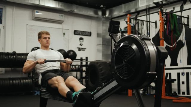 Fitness young man using rowing machine in the gym crossfit training at night student professional athlete bodybuilder