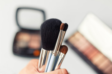 Set of makeup brushes in female hand on the background of eye shadow sets