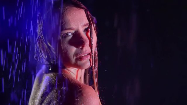 close up. portrait of a sad young woman in neon color in the dark under the streams of rain. cold drops run down the hair and skin