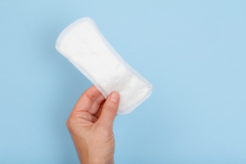 Woman's hand with white sanitary napkin on a blue background.