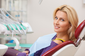 Relaxed beautiful woman smiling over her shoulder to the camera, sitting in dental chair, waiting for medical appointment with her dentist. Happy patient at dental clinic. Dentistry service concept