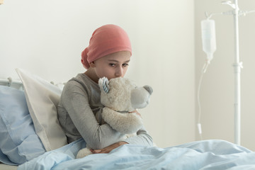 Weak sick girl with headscarf hugging teddy bear next to drip in the medical center © Photographee.eu