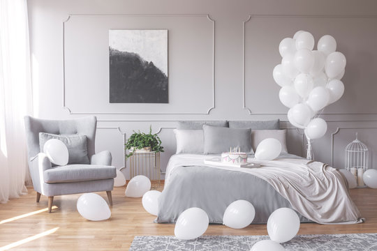 Real photo of a romantic bedroom interior with an armchair, double bed and balloons
