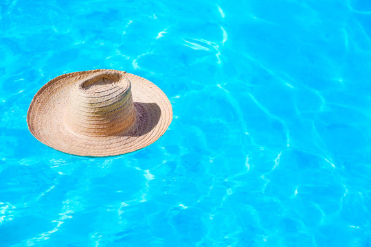 Straw hat on the surface of blue clear swimming pool with free space. Summer vacation concept.