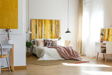 Floral pillow and pastel pink sheets on comfortable bed in contemporary bedroom interior with fancy...
