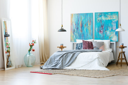 Two abstract blue painting as headboard of comfortable king size bed with white and grey bedding