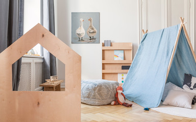 Wooden desk and blue tent with pillows in child's playground interior with pouf and poster. Real...