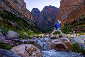 Girl with a backpack crosses the river in the mountains.