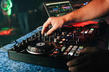 hands of a DJ in a booth playing on the mixer in the club