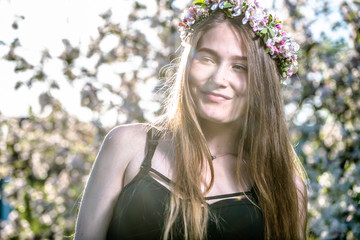 Beautiful smiling innocent pure girl in a wreath with flowers of white apple blossom, spring outdoor portrait of woman face with arms