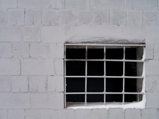Old window with bars on a snowy frozen wall