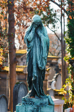 Grieving statue in an old European Catholic cemetery at sunset.