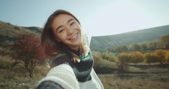 Smiling charismatic young lady with brackets in front of the camera holding with one hand and capturing some memories of amazing trip.