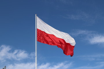 White-red horizontal flag on a flagpole developing in the wind against a blue sky with light clouds. Symbol of the Polish state.