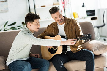 teen son teaching father play acoustic guitar at home