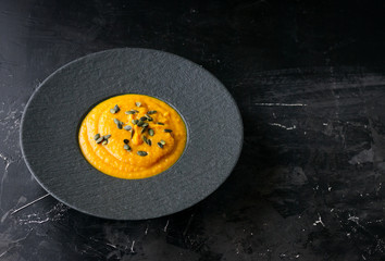 Pumpkin orange cream soup in black plate. Dark photo
