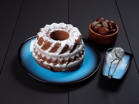 Delicious chestnut bundt cake using sweetened chestnut purée and chocolate chips, dusted with sugar, set on a blue plate, on a dark brown background