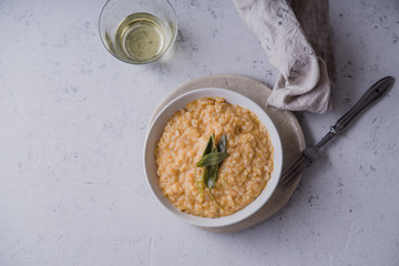 Pumpkin risotto with parmesan and sage served with a glass of white wine. Overhead view, concrete background, copy space