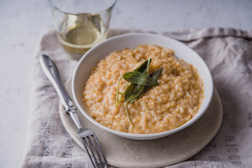 Pumpkin risotto with parmesan and sage served with a glass of white wine. Side view, concrete background