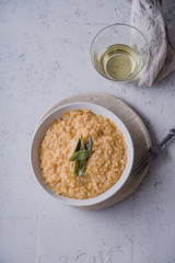 Pumpkin risotto with parmesan and sage served with a glass of white wine. Overhead view, concrete background