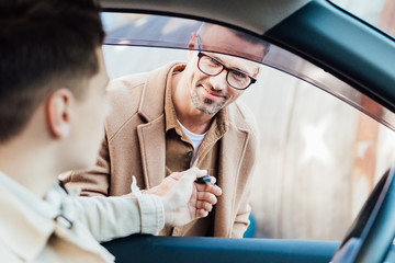 handsome cheerful father giving car key to teen son on street