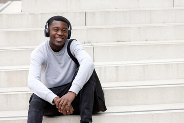 happy young african man sitting on steps and listening to music with headphones