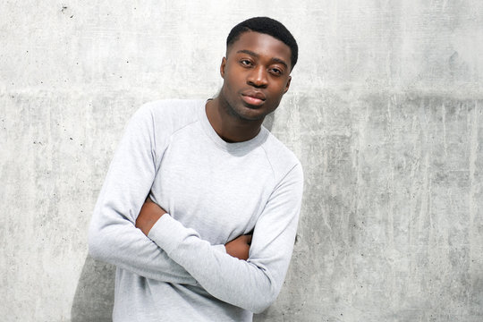 cool young black man posing with arms crossed against gray wall