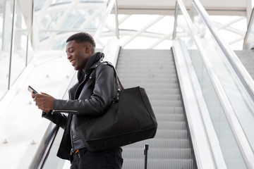 young black man with cellphone and bag on escalator at station