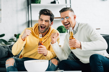 excited son and mature father watching sport with beer on weekend at home