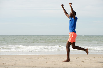 side portrait of happy young man running at beach with arms raised