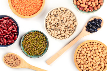 Various types of legumes, shot from above on a white background. Red kidney and pinto beans, lentils, chickpeas, soybeans, black-eyed peas