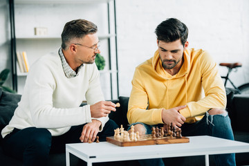 son and mature father playing chess together on weekend in living room