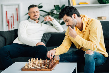 young son and mature father playing chess on weekend at home