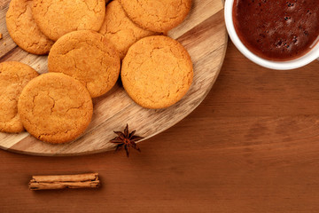 A photo of ginger cookies with a mug of hot chocolate, a cinnamon stick, and an anise star, shot from the top on a dark rustic background with a place for text